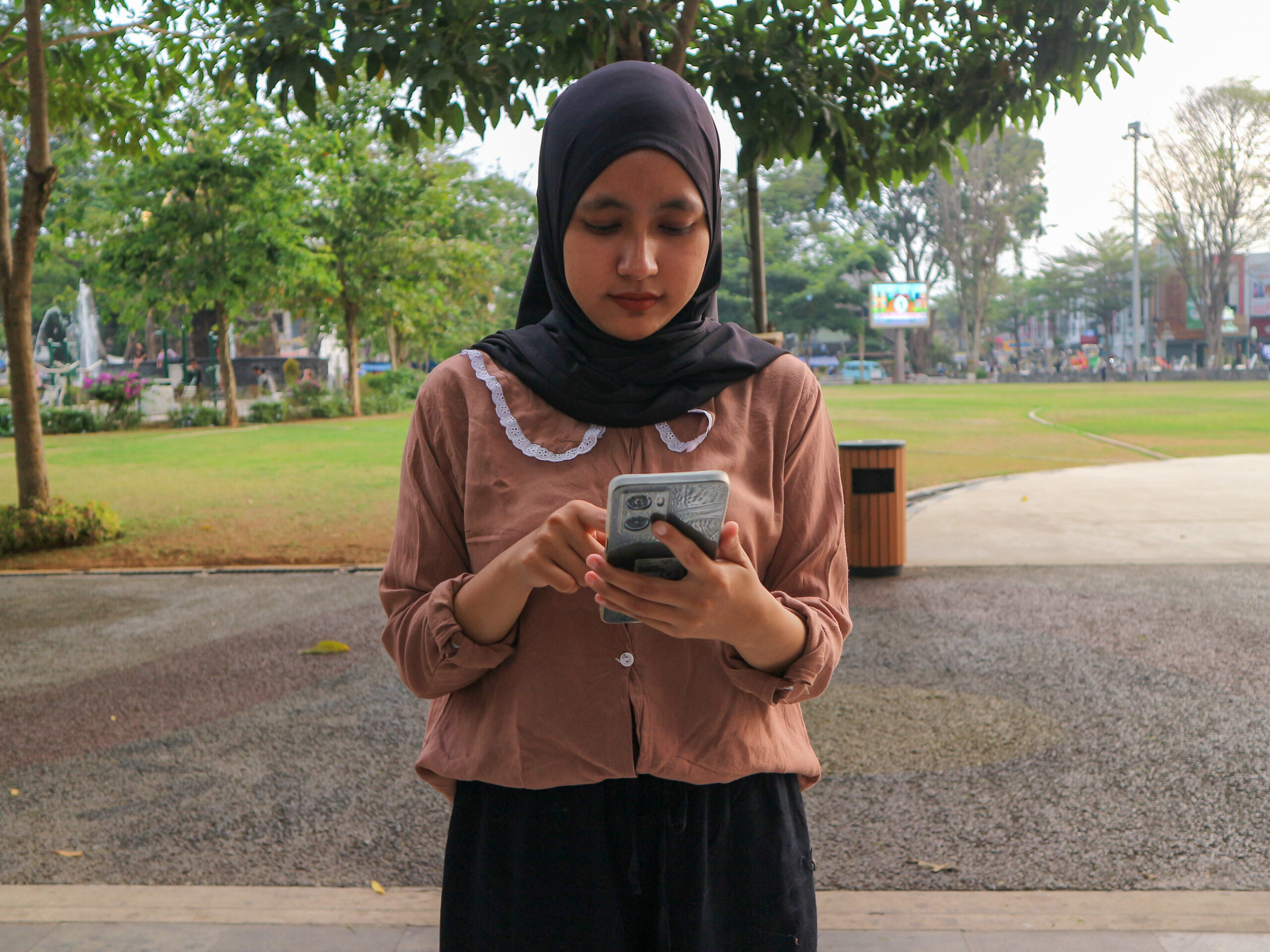 portrait of muslim woman using mobile phone reading message at city park. enjoying, relaxing weekend